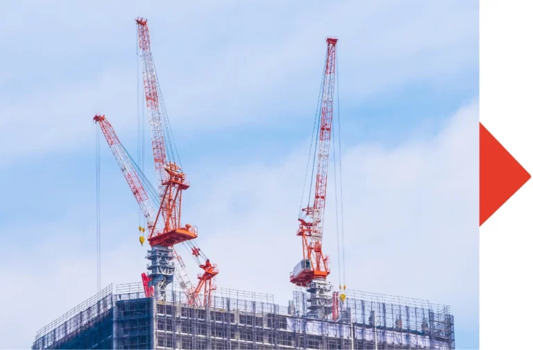 Imagen del proceso de una obra, se pueden ver dos grandes grúas rojas en la cima de un edificio.